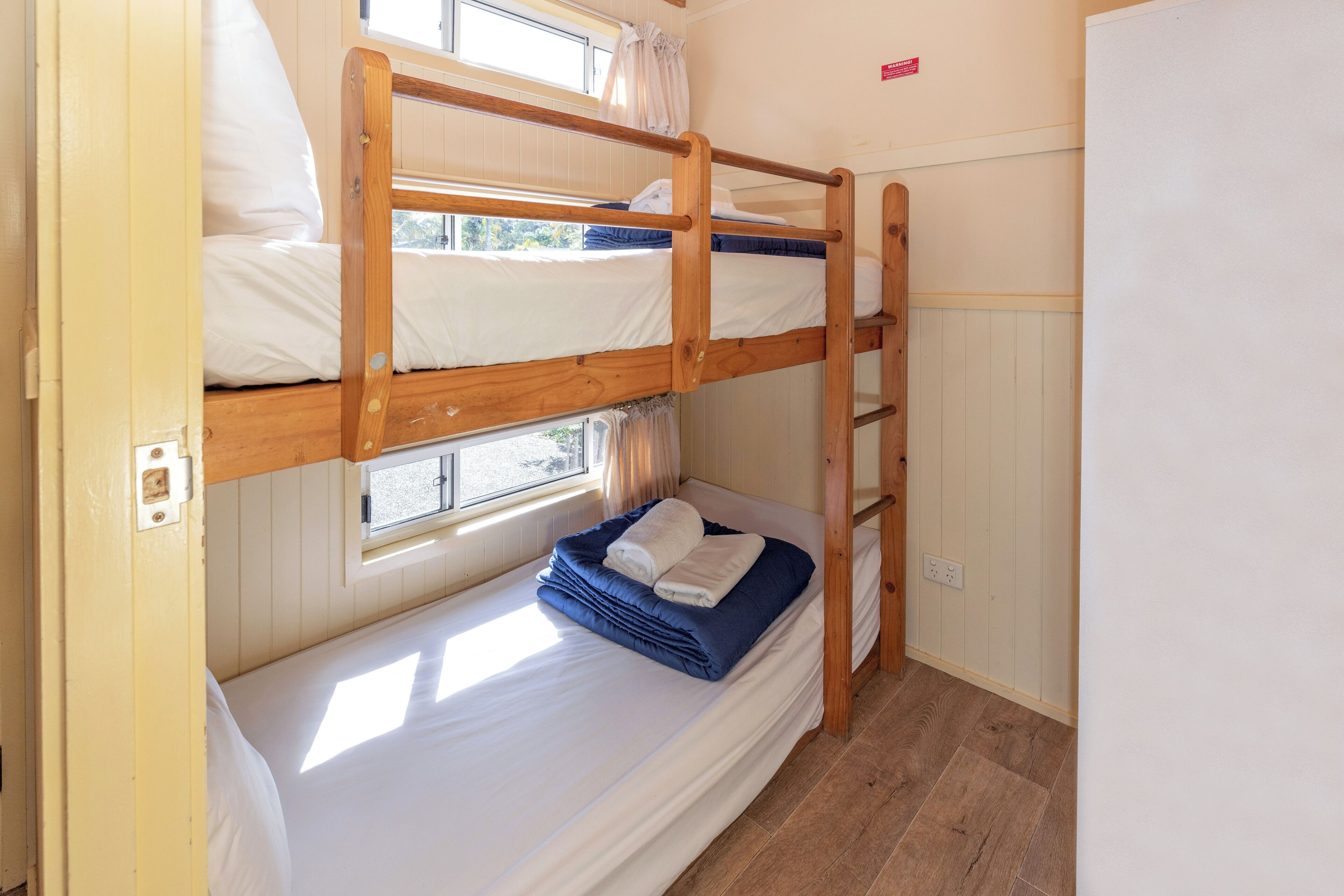 A bunk bed room with a window, wooden bunk beds, and a ladder.