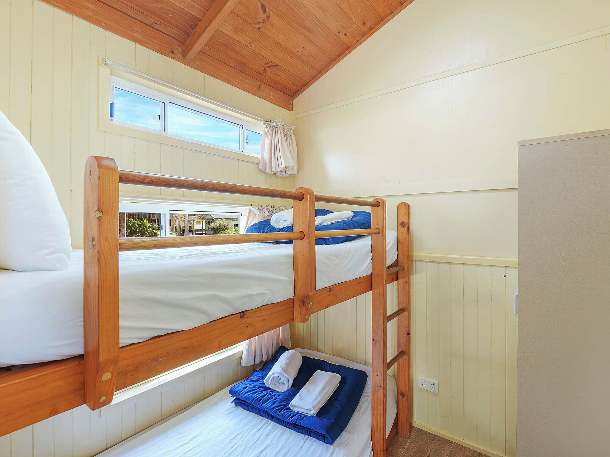 Une chambre avec un lit superposé doté de barrières en bois, une fenêtre avec des rideaux et un radiateur.