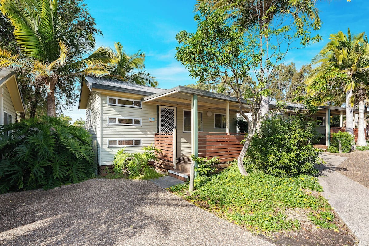 A single-story house with a porch, surrounded by lush greenery and palm trees.