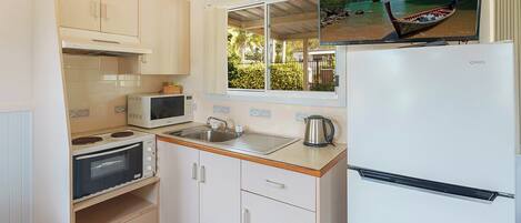 A compact kitchen with white cabinets, a microwave, a stove, a sink, and a refrigerator.