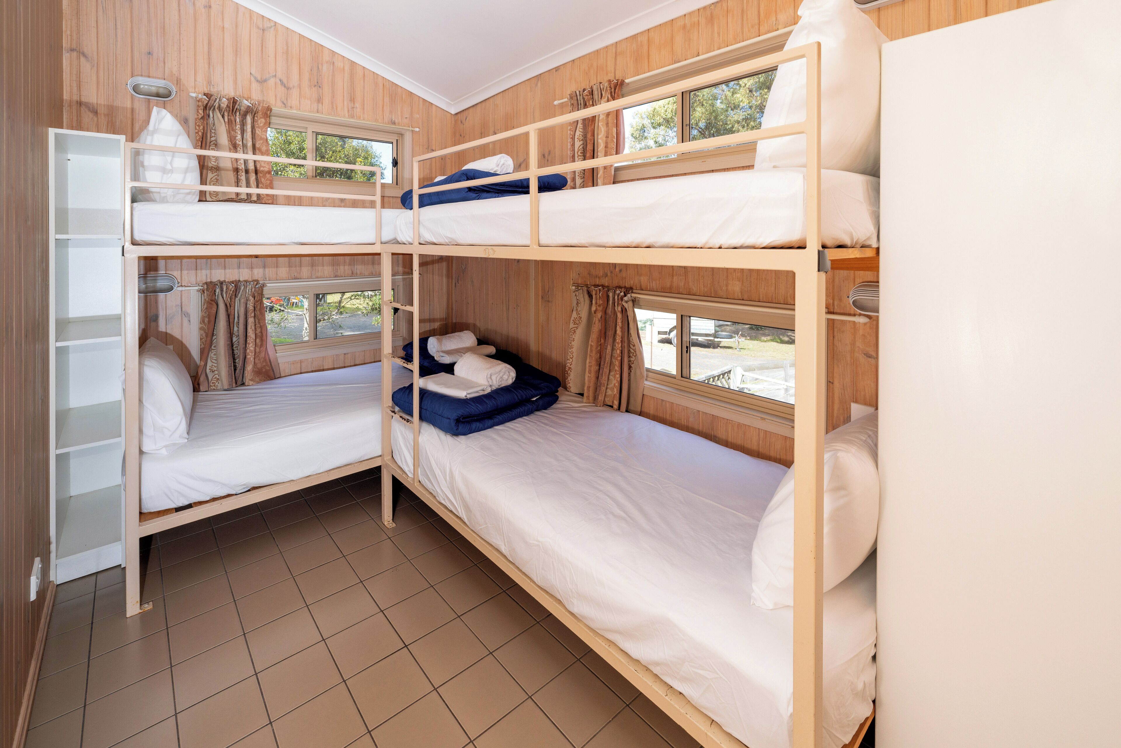 Une chambre avec trois lits superposés, une armoire blanche et une fenêtre avec des rideaux.