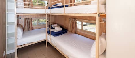 Une chambre avec trois lits superposés, une armoire blanche et une fenêtre avec des rideaux.