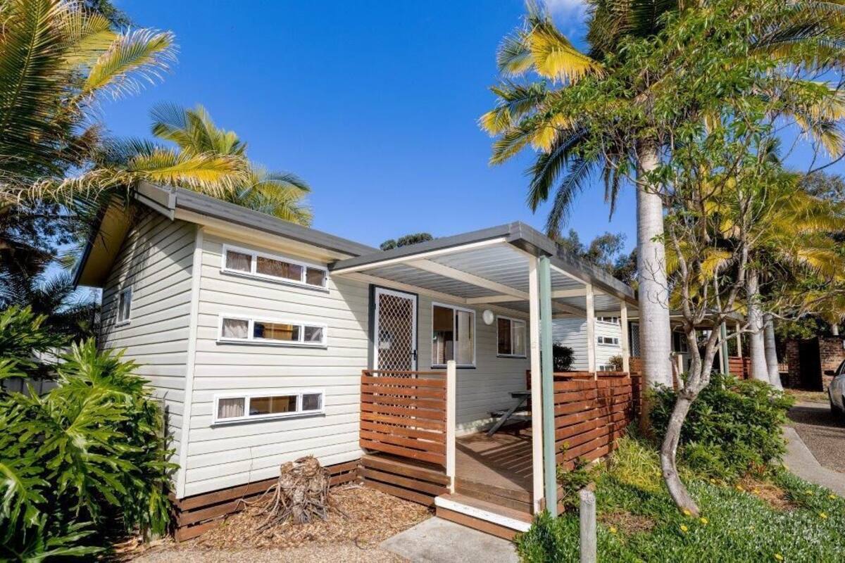 A single-story house with a covered porch, surrounded by palm trees and a well-maintained garden.