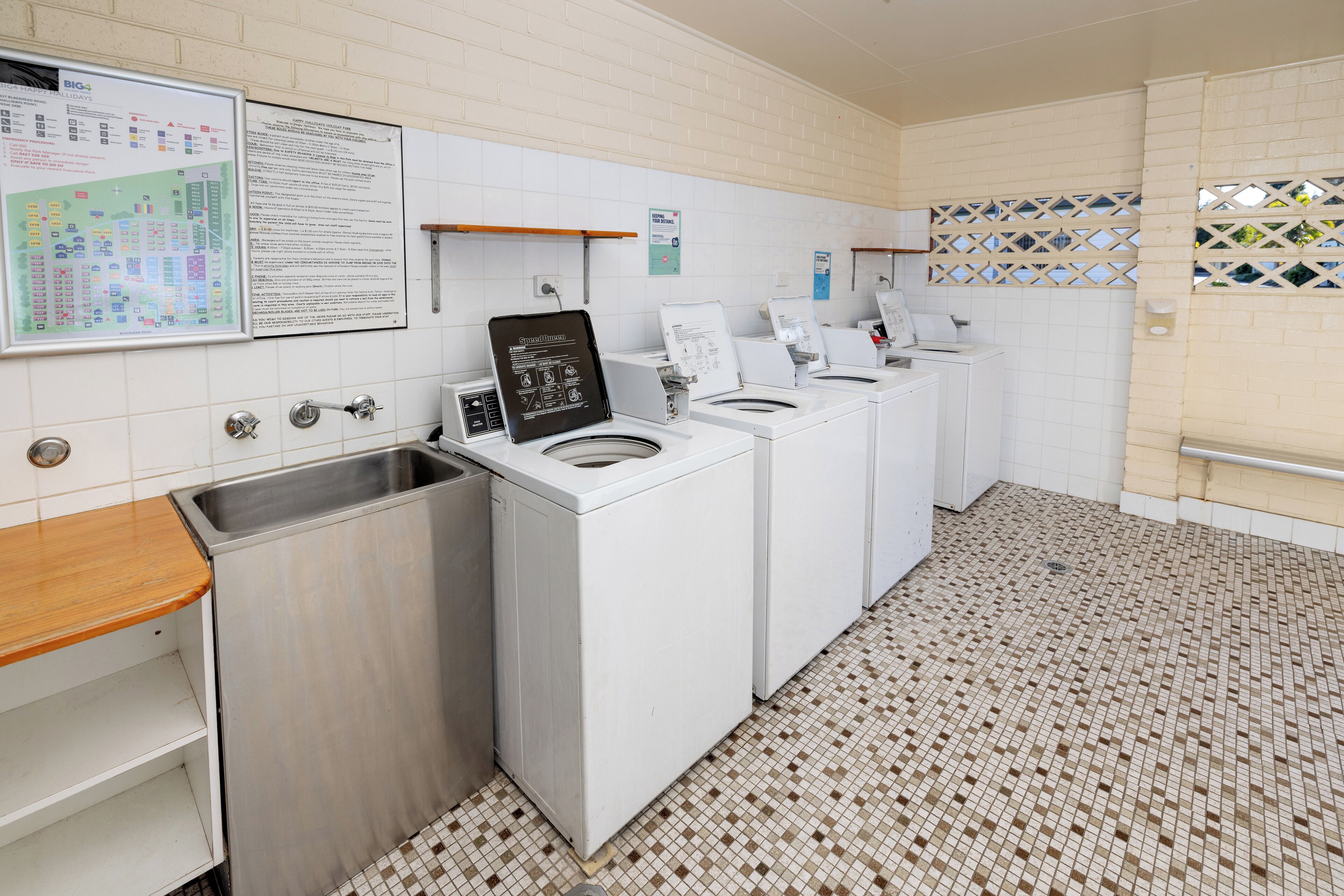 A laundry facility with multiple washing machines, a sink, and informational posters on the wall.