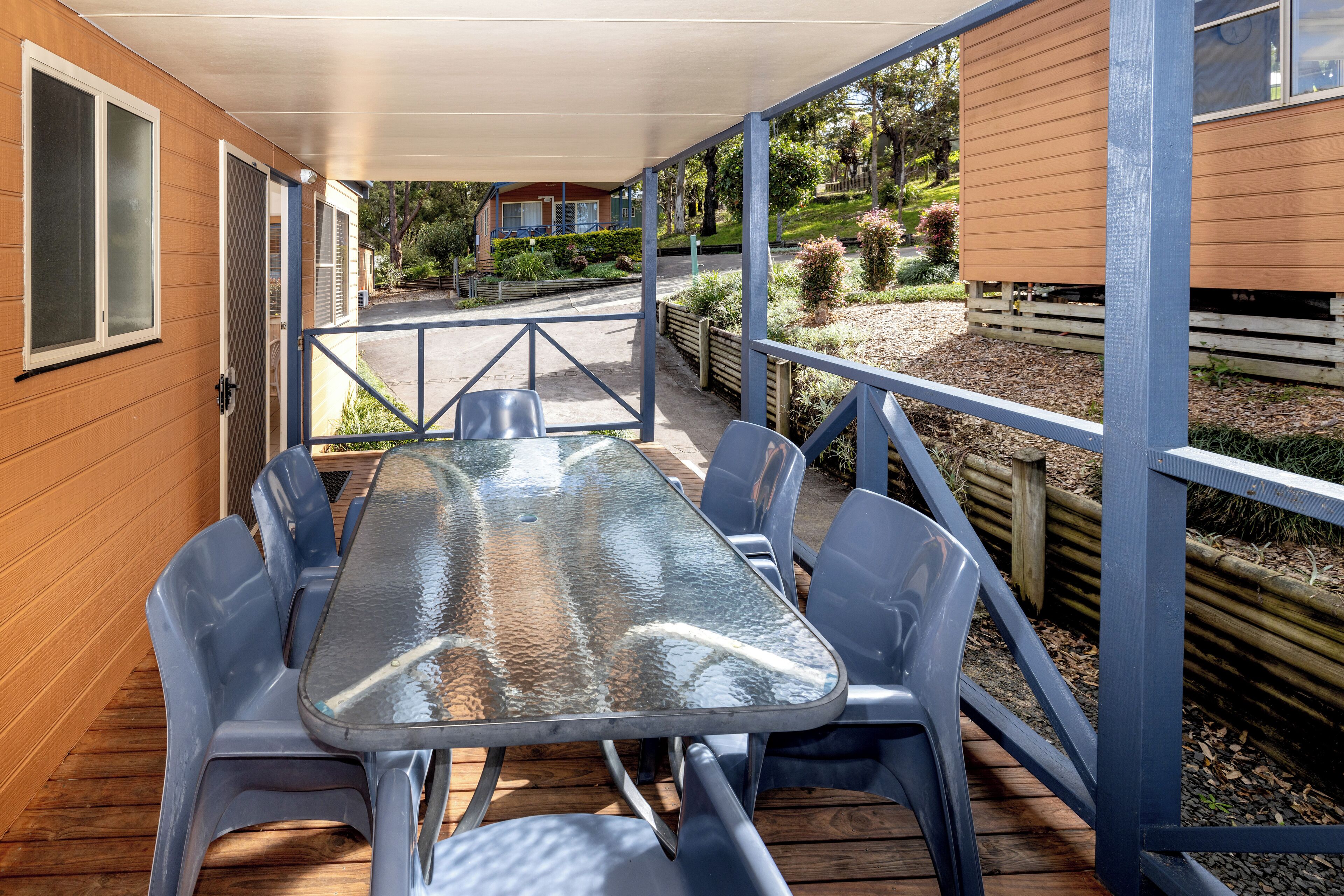Una veranda esterna coperta con un tavolo in vetro e sedie di plastica blu.