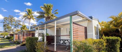 A modern, single-story house with a covered porch, surrounded by lush greenery and palm trees.