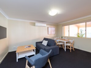 A modern living room with a grey sofa, a wooden coffee table, a dining table with chairs, and a large window with a view. - Villa Nova (South Toowoomba)