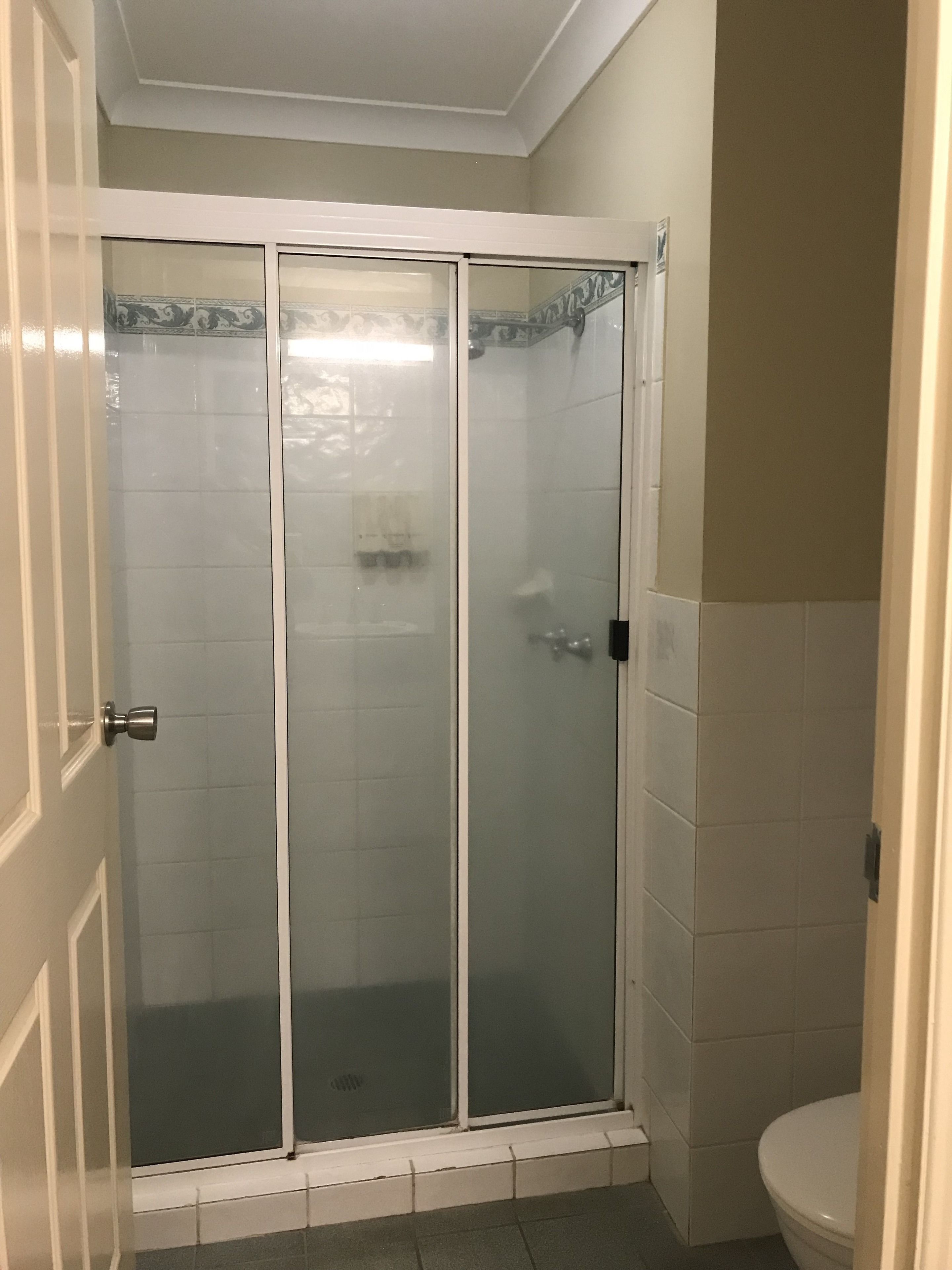 A bathroom with a glass-enclosed shower, a toilet, and a door with a handle.
