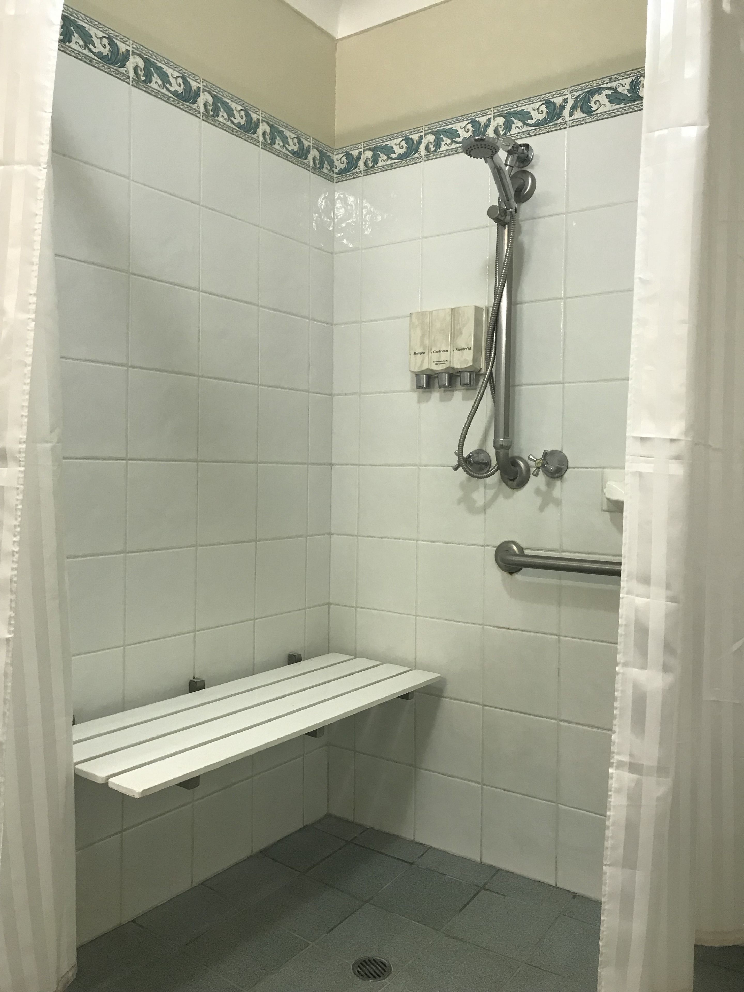 A shower with a bench, a handheld showerhead, and a wall-mounted faucet.
