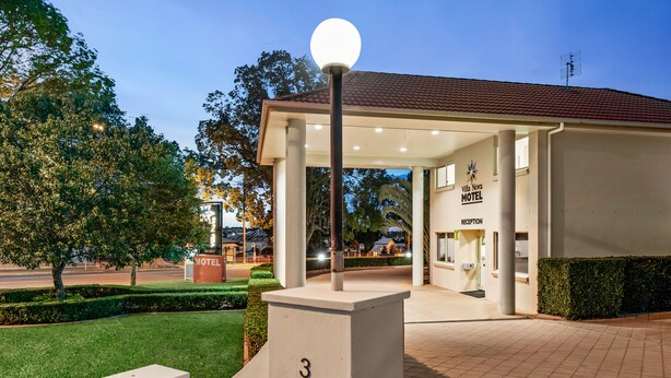 A modern hotel entrance with a covered reception area, a well-maintained lawn, and a clear sky. - Villa Nova (South Toowoomba)