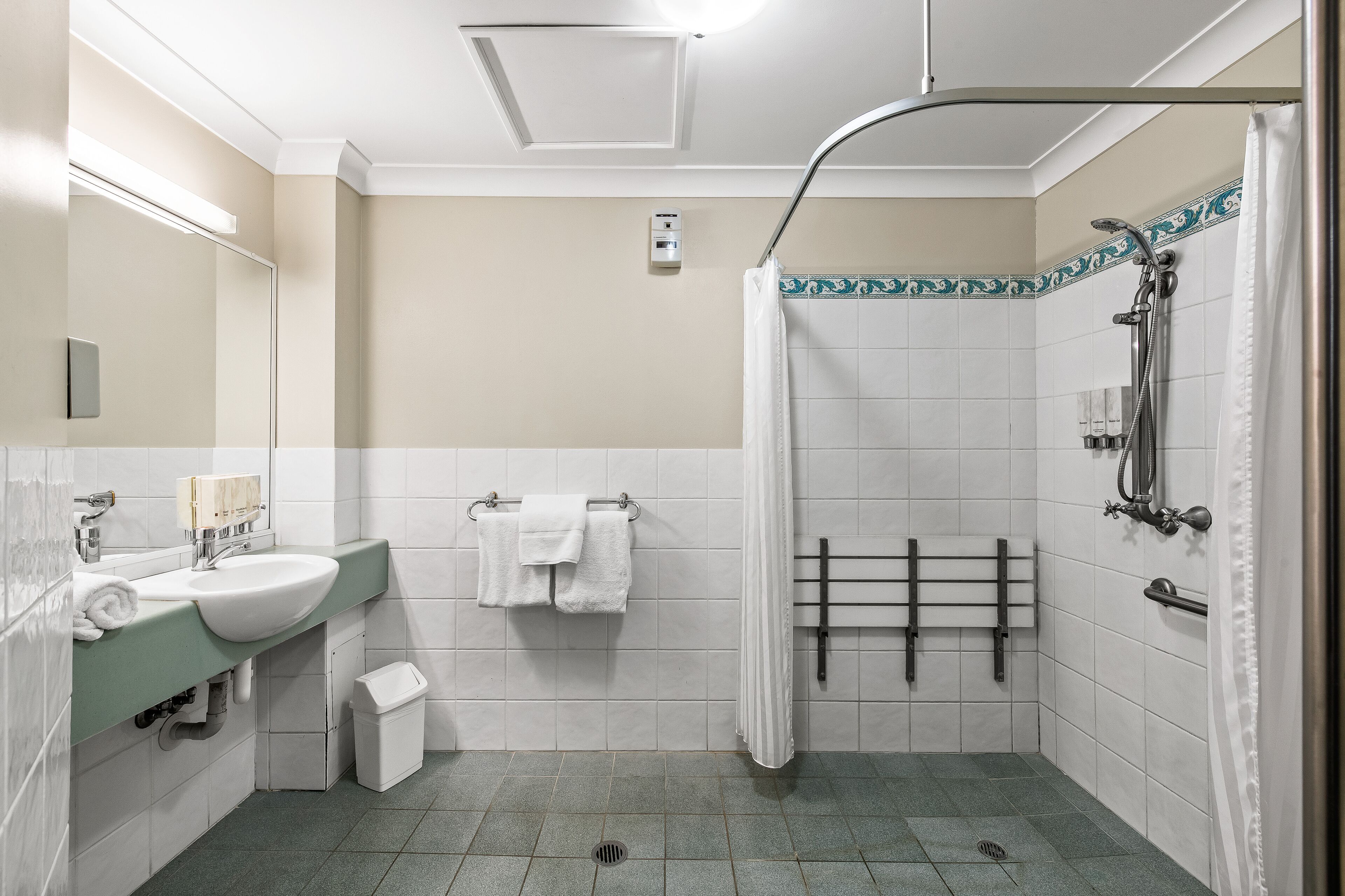 Ein modernes Badezimmer mit Waschbecken, Spiegel, Handtuchhalter, Dusche und gefliesten Wänden.