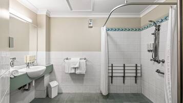 Ein modernes Badezimmer mit Waschbecken, Spiegel, Handtuchhalter, Dusche und gefliesten Wänden.