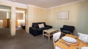 A modern living room with a sofa, armchairs, a coffee table, and a dining area with a table set for two. - Villa Nova (South Toowoomba)