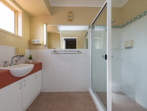 A modern bathroom with a sink, mirror, and glass shower enclosure. - Villa Nova (South Toowoomba)