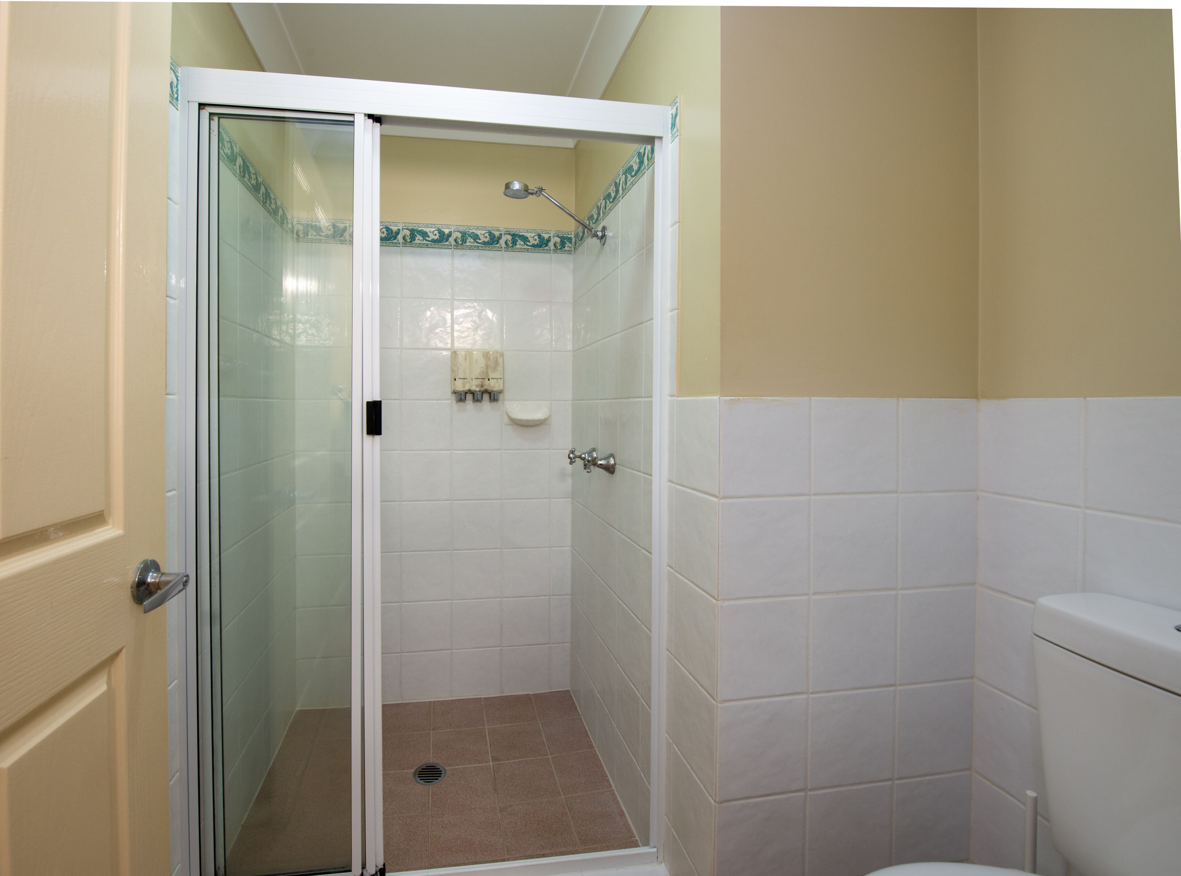 Un bagno con doccia vetrata, piastrelle bianche e parete color beige.