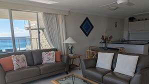 Una sala de estar con sofá, sillón, mesa de centro y vista al océano.
