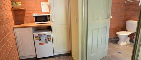 A compact kitchen with a microwave, refrigerator, and a small shelf with snacks.