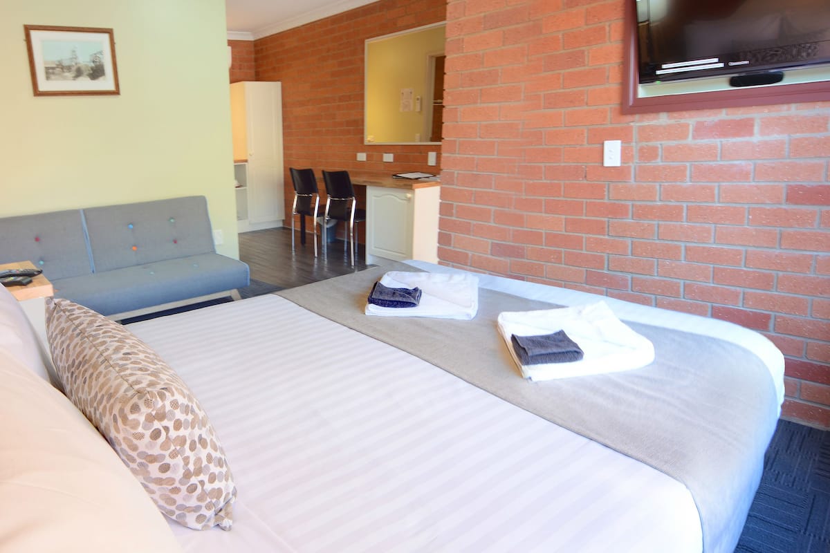 Habitación de hotel con cama, escritorio y televisor montado en la pared de ladrillo.