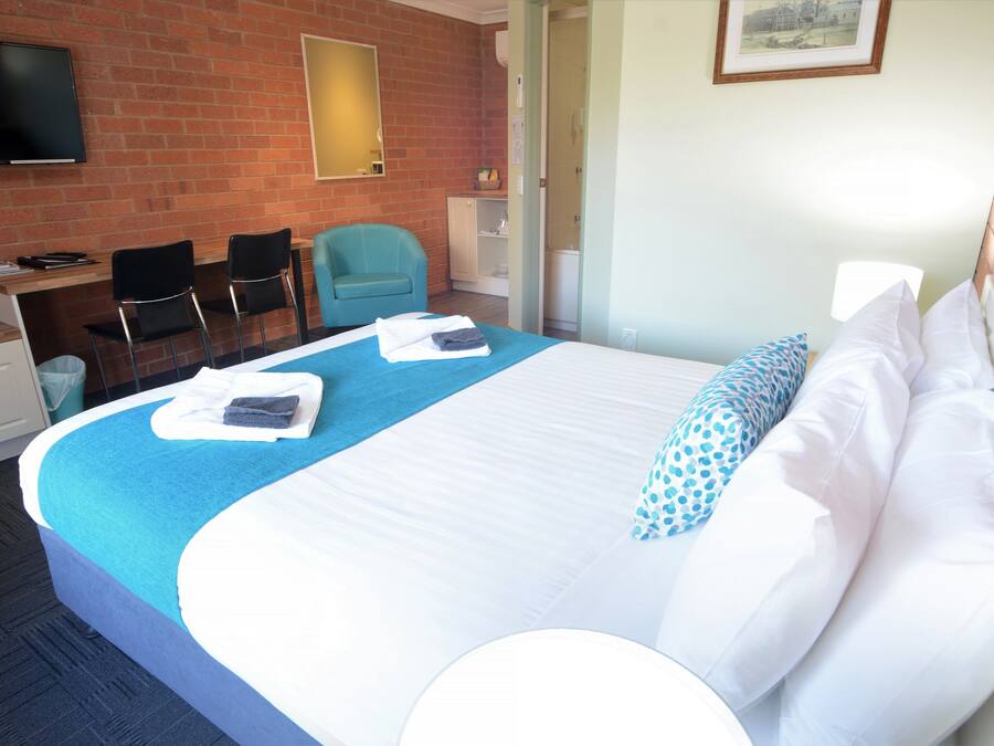 Habitación de hotel con una cama grande, un escritorio con dos sillas, un televisor y un baño visible a través de una puerta abierta.