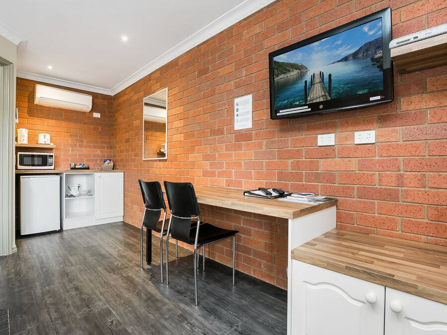 A modern kitchen with a brick wall, a flat-screen TV, and a wooden countertop.