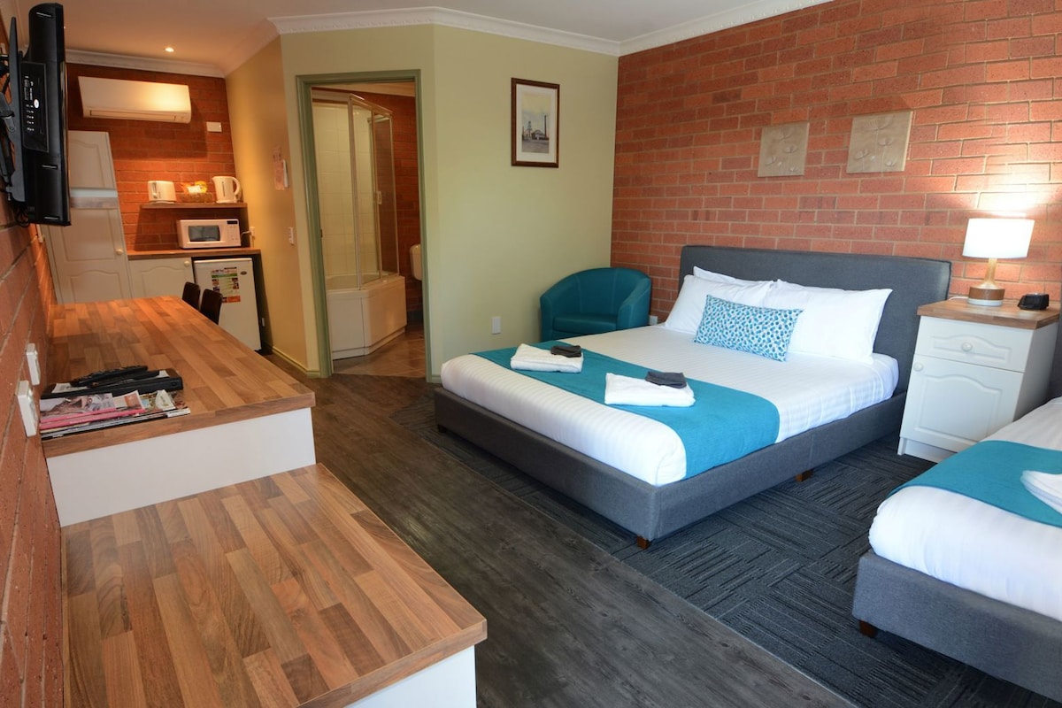 A hotel room with two beds, a desk, a microwave, and a shower.