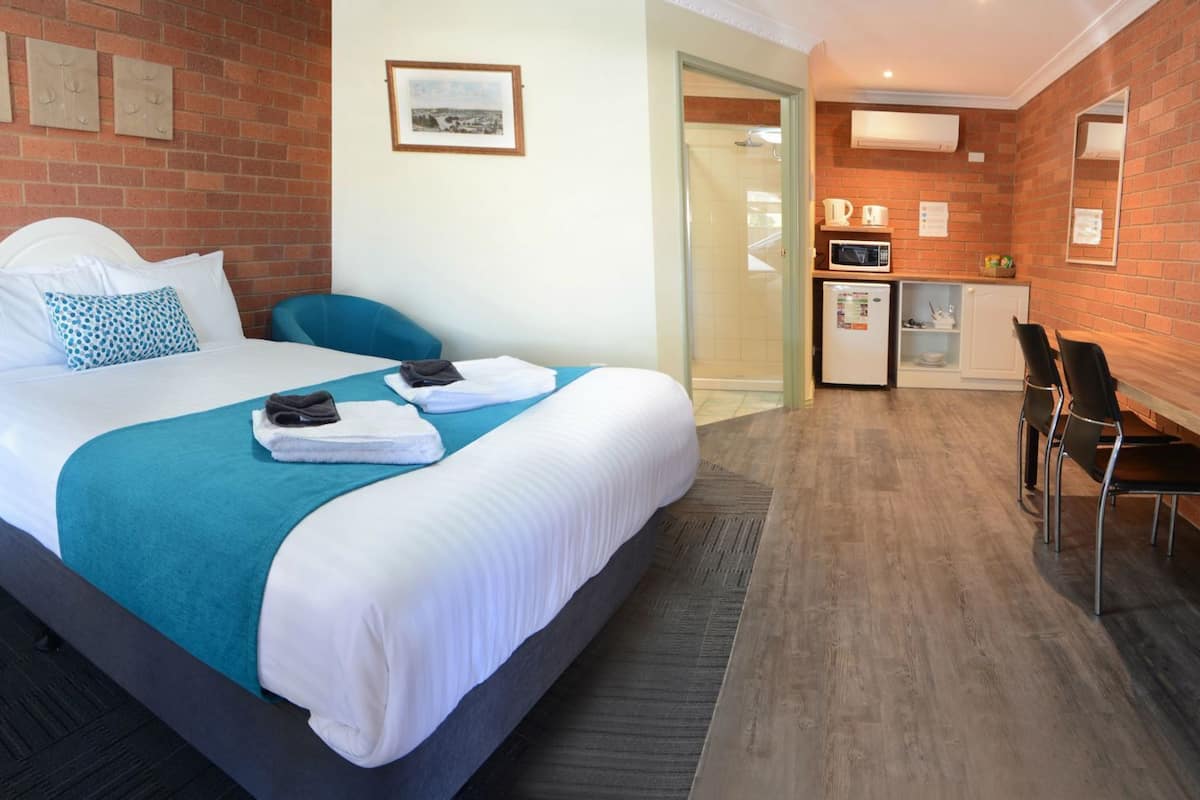 Habitación de hotel con cama, escritorio, silla, microondas y refrigerador.