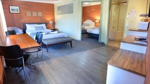 Habitación de hotel con cama, mesita de noche, silla y una pequeña zona de kitchenette.