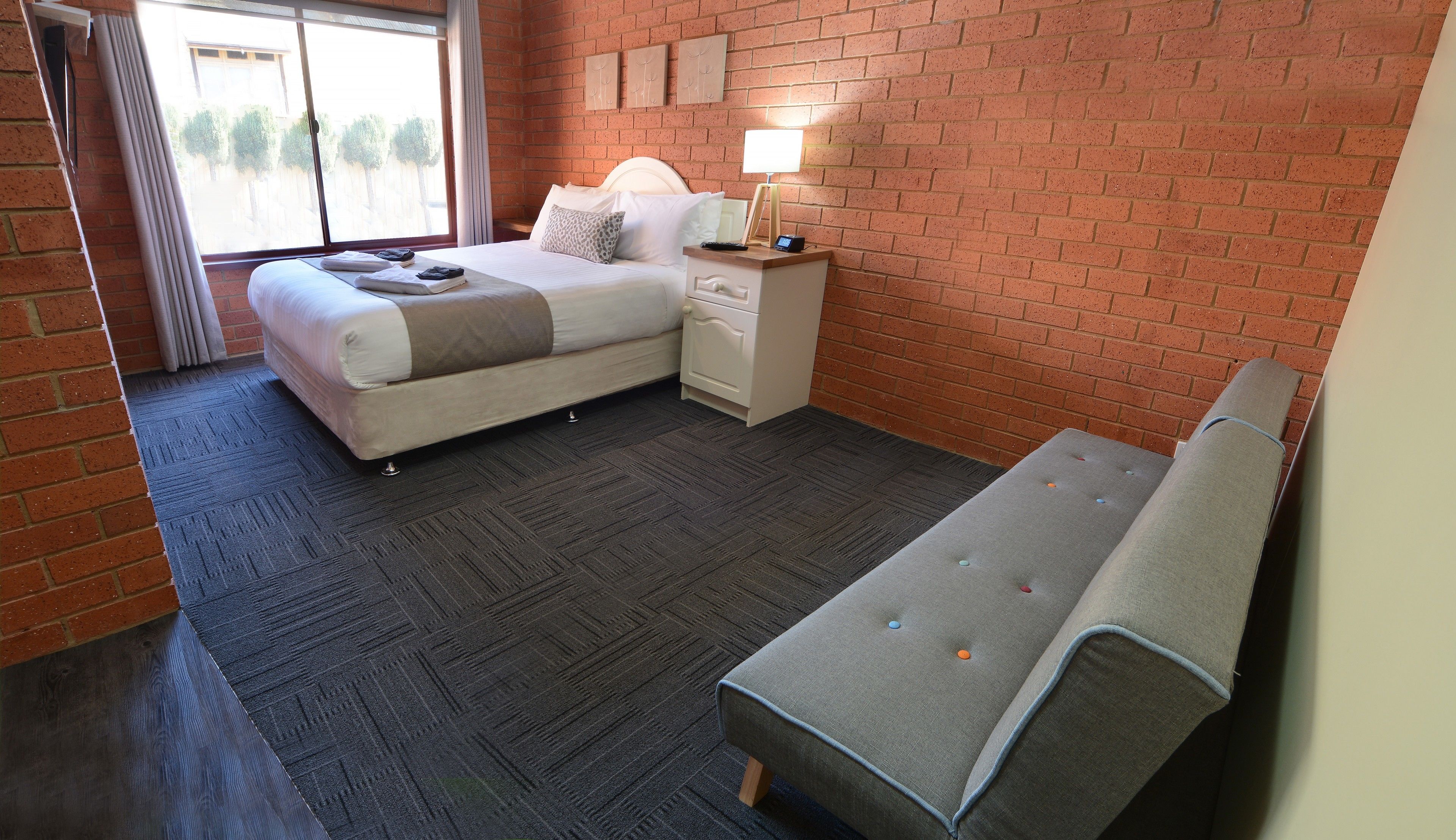 Un dormitorio con cama, mesita de noche, lámpara y un banco.