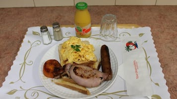 Un plato de huevos revueltos, salchichas y carne a la parrilla sobre una mesa con una servilleta decorativa y saleros y pimenteros.