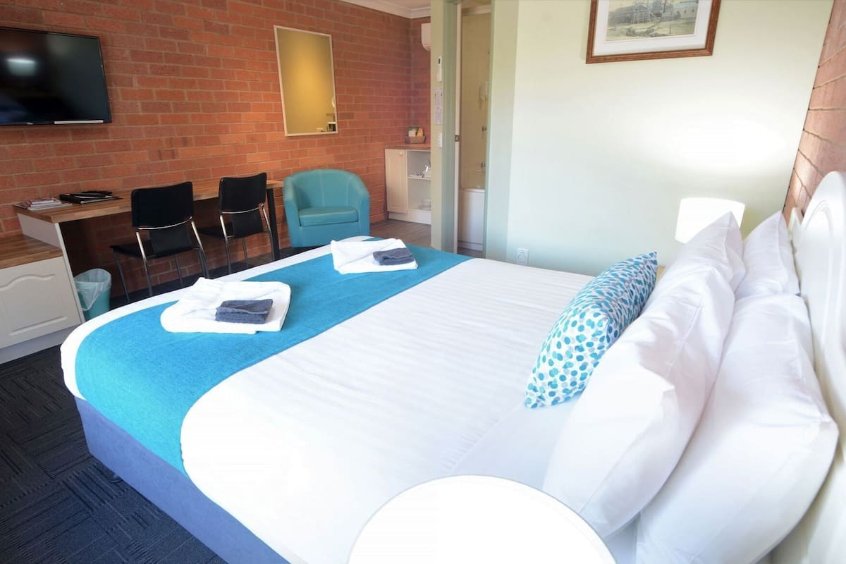 Una habitación de hotel con cama, escritorio, silla, televisor y baño.