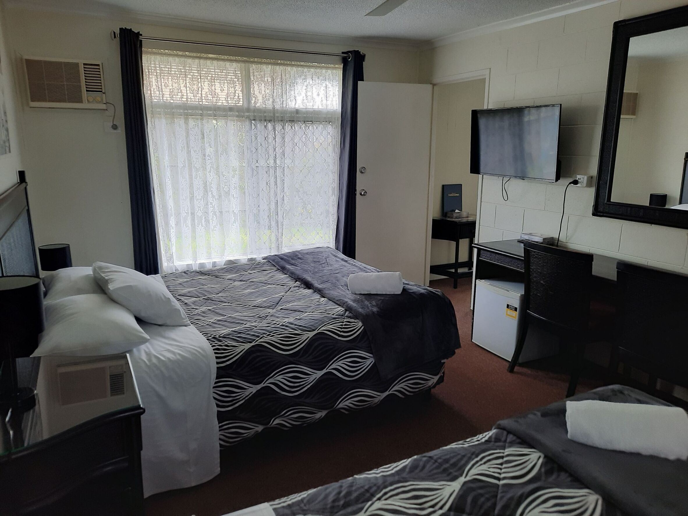 A hotel room with a bed, a desk, a chair, a TV, and a window with curtains.