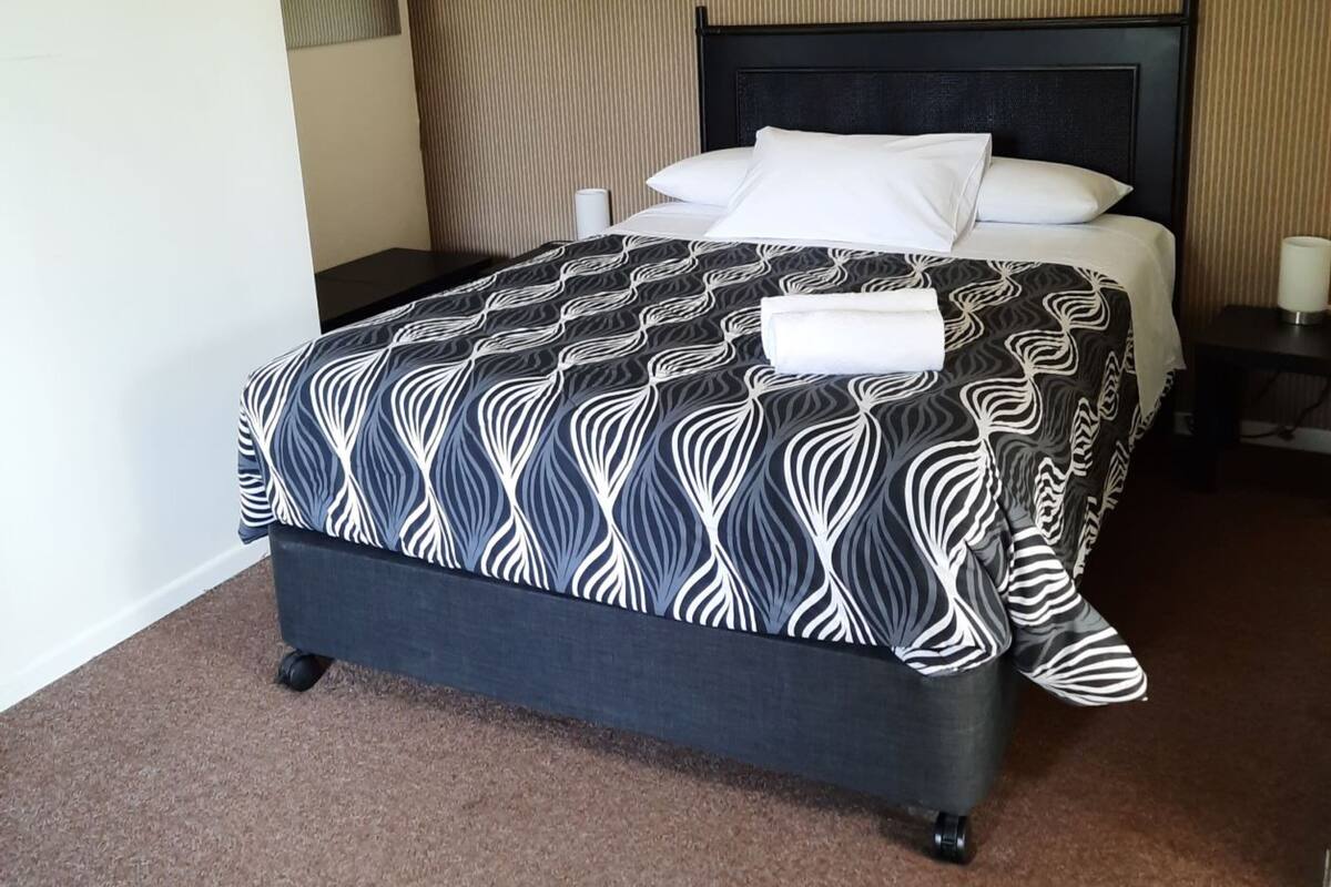 Une chambre d’hôtel avec un lit, une table de chevet, une lampe et un mur orné d’un motif texturé.