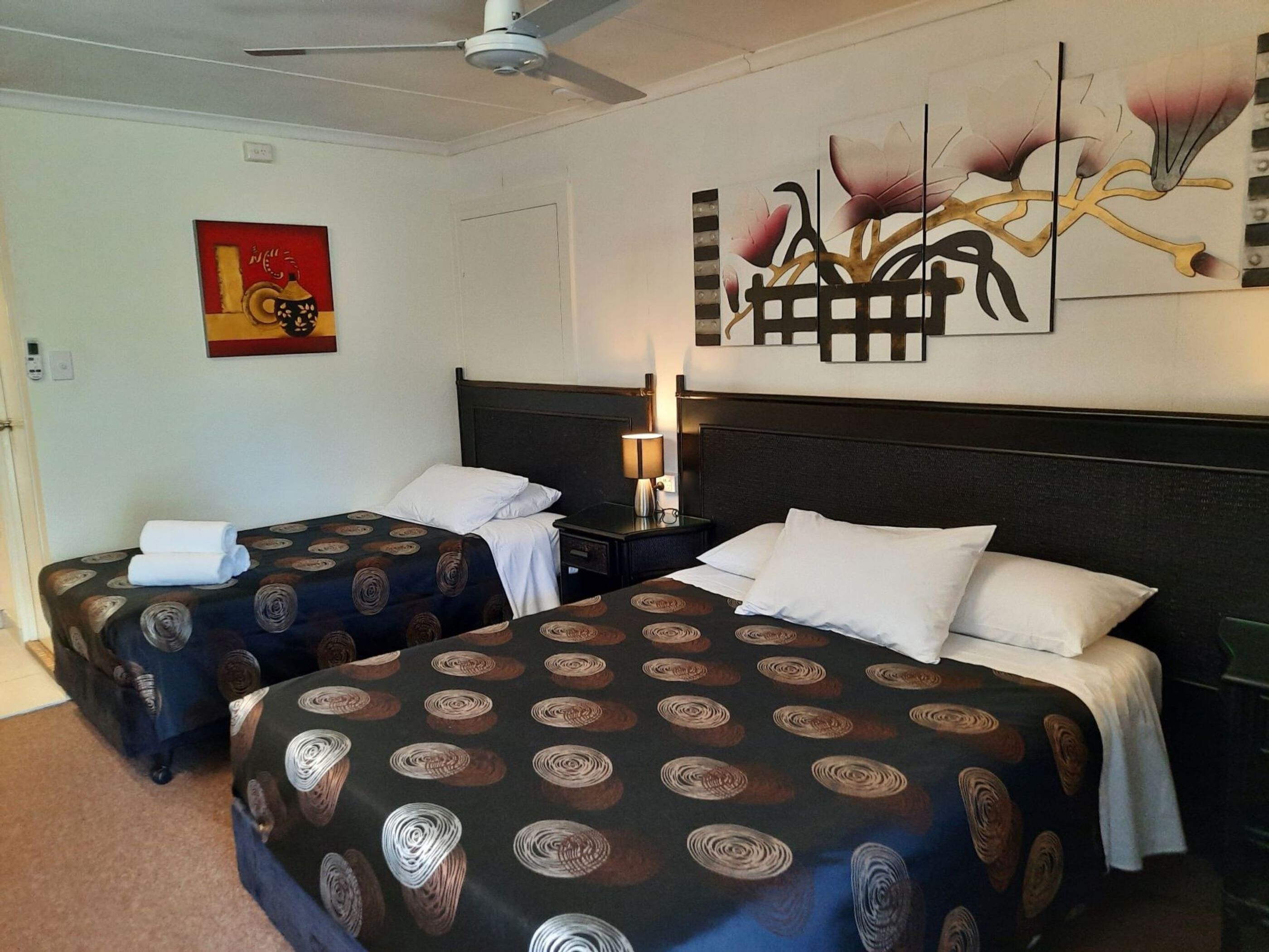 A hotel room with two beds, each with patterned bedding, a nightstand with a lamp, and a ceiling fan.