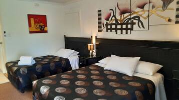 Habitación de hotel con dos camas, cada una con ropa de cama estampada, una mesita de noche con lámpara y un ventilador de techo.
