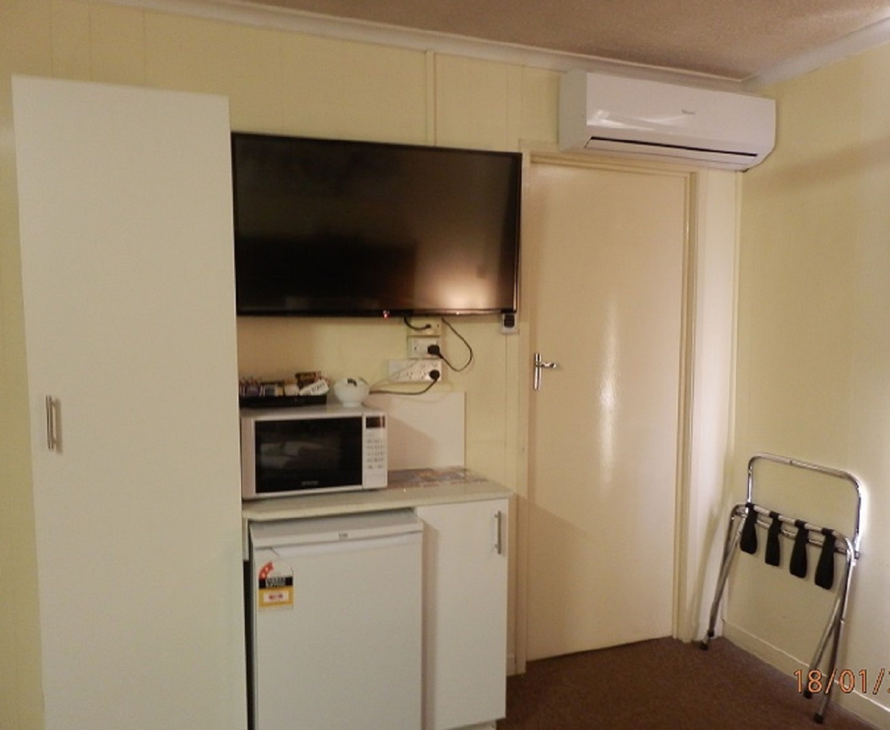 Una kitchenette compacta con microondas, un refrigerador pequeño y un televisor de pantalla plana sobre la encimera.
