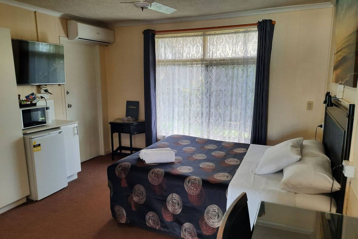 Une chambre d’hôtel de taille réduite, équipée d’un lit, d’un petit bureau, d’un four à micro-ondes et d’un appareil de climatisation.