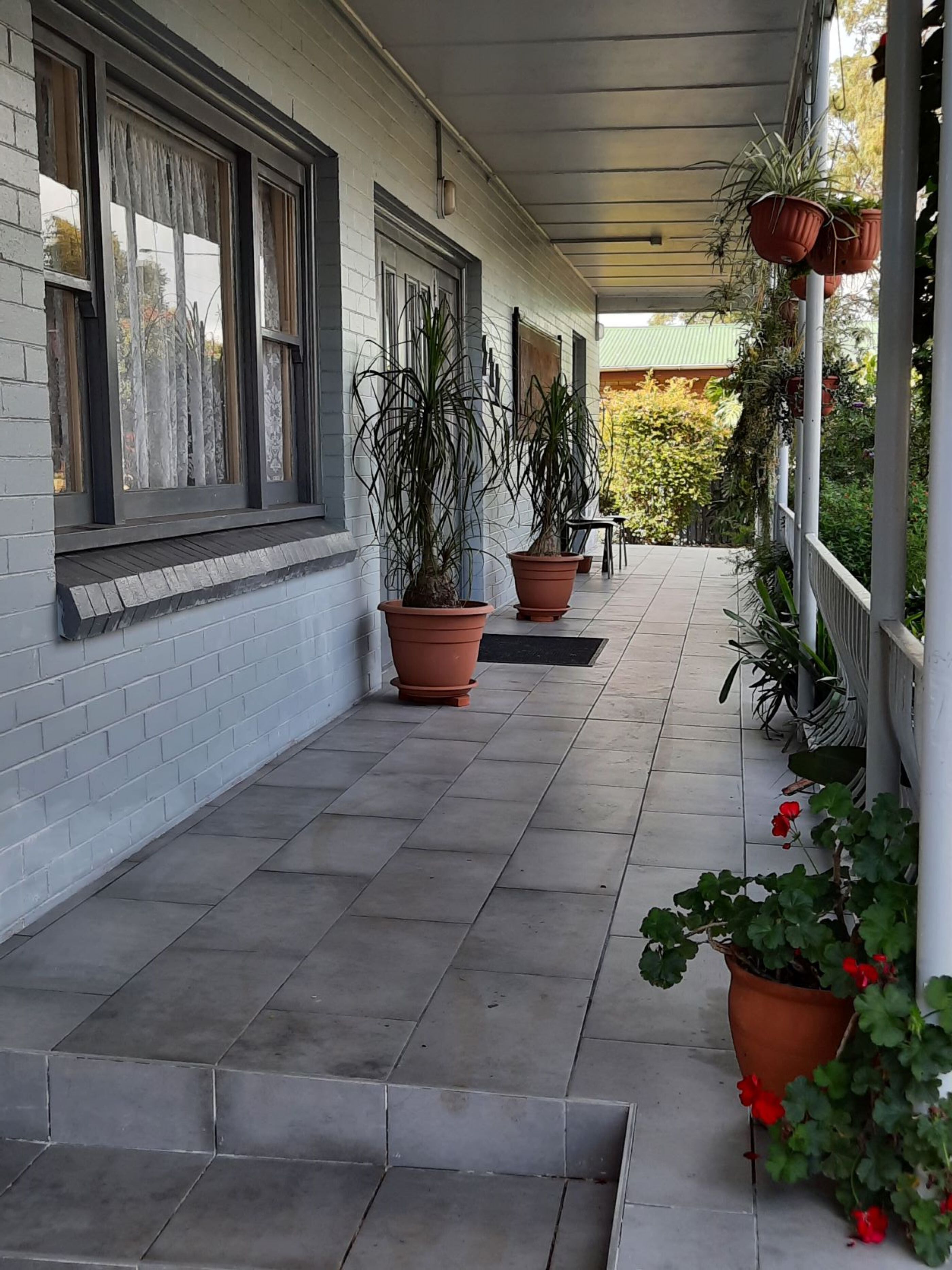 A covered porch with potted plants and a tiled floor.