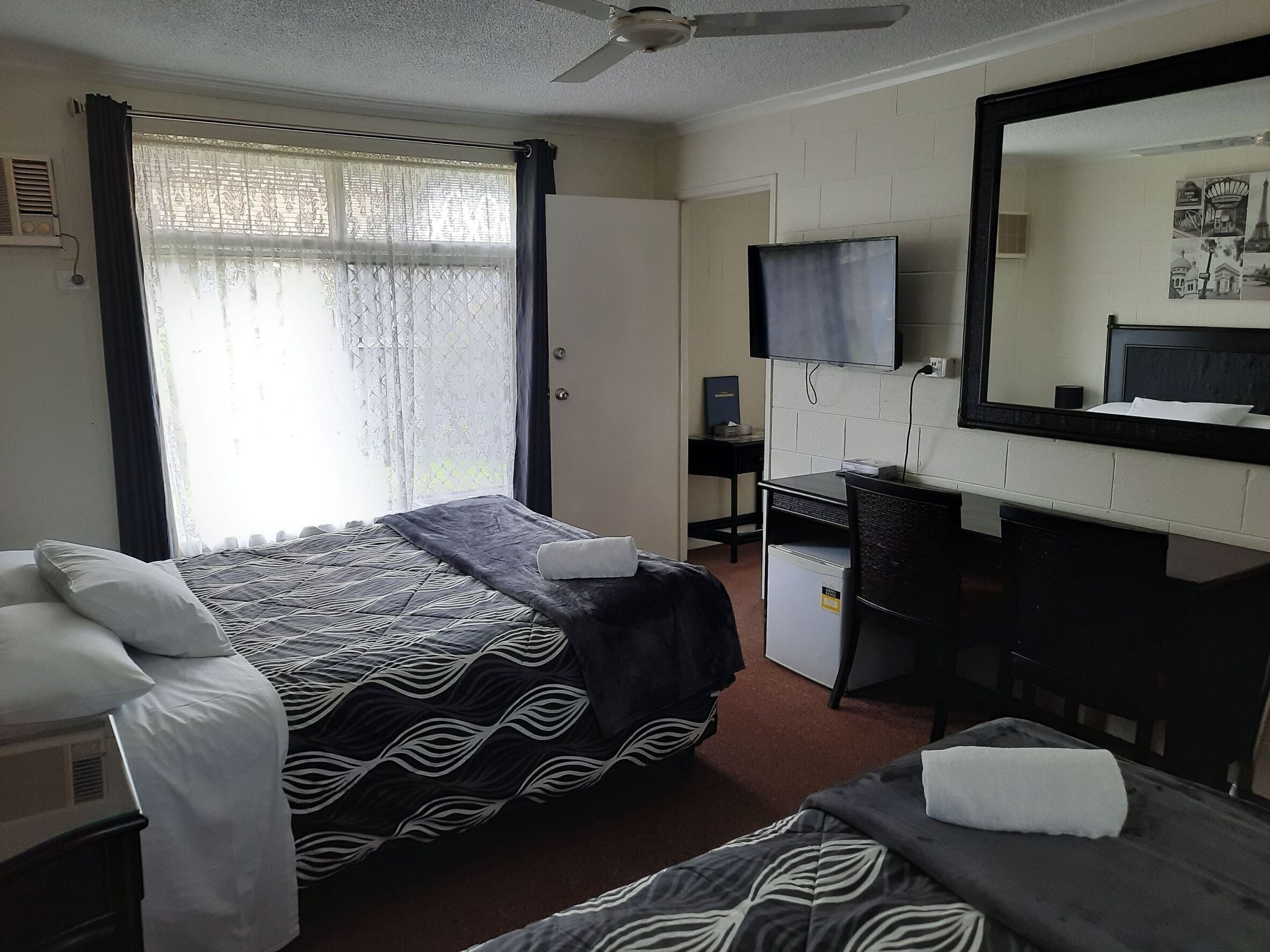 A hotel room with a bed, a desk, a chair, a mirror, and a ceiling fan.