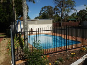 A swimming pool surrounded by a black metal fence, with a white building in the background and trees around. - Flying Spur Motel (Wilsonton)