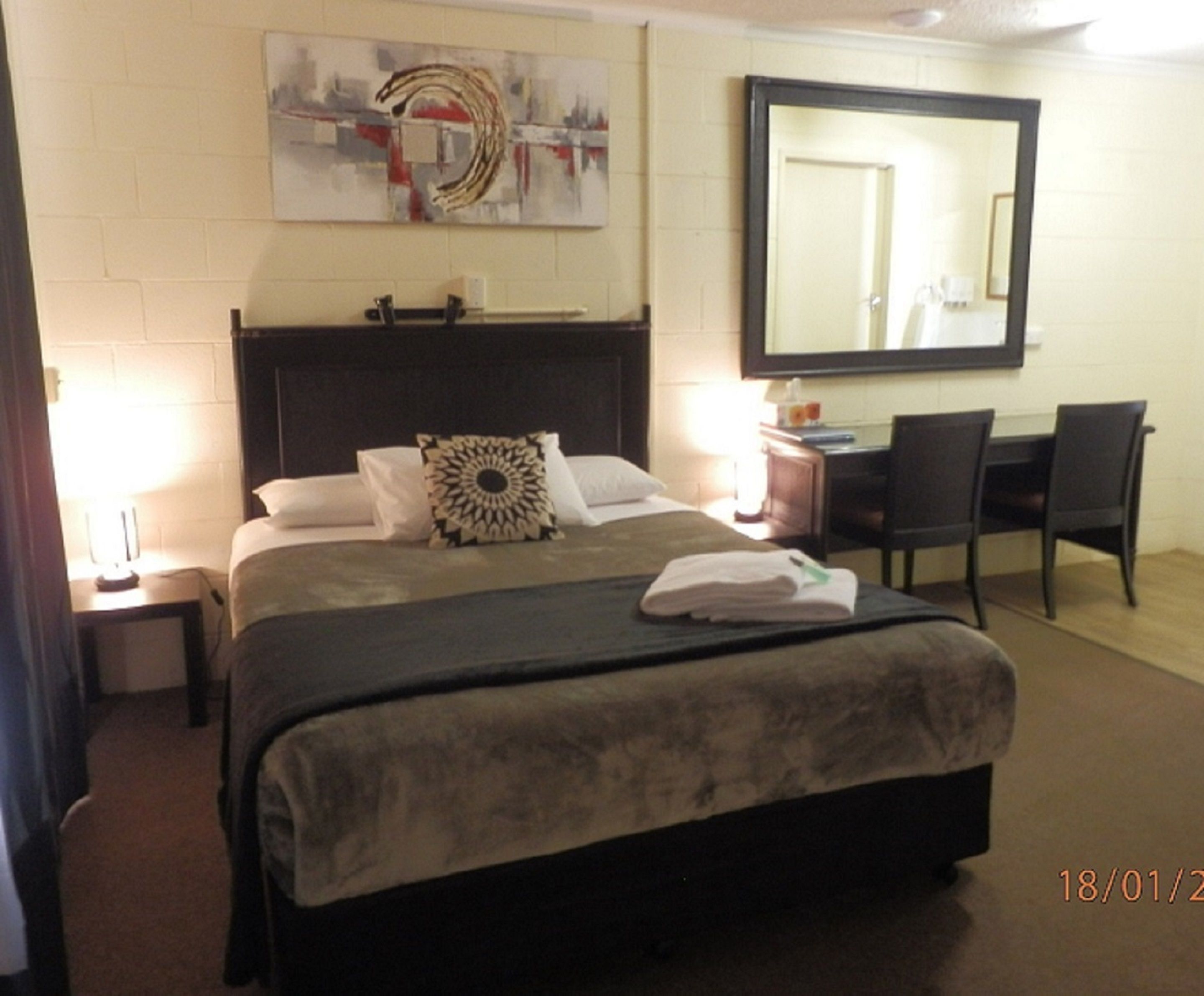 Une chambre d’hôtel avec un lit, un bureau, une chaise, un grand miroir et un tableau au mur.
