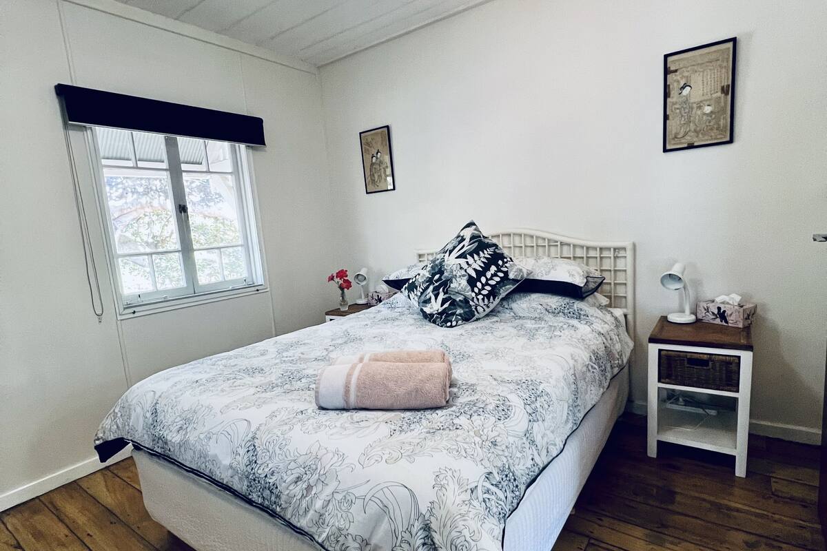 A bedroom with a bed, a nightstand, a ceiling fan, a window, and a wall-mounted picture.