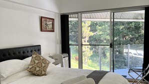 A bedroom with a large bed, a ceiling fan, a window with a view of greenery, and a chair by the window. - Ingleside Stud Farm (Tallebudgera Valley)
