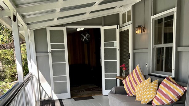 A covered porch with a gray couch, striped pillows, and a round metal table. - Ingleside Stud Farm (Tallebudgera Valley)