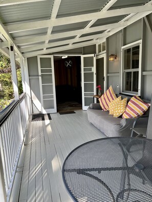 A covered porch with a gray couch, striped pillows, and a round metal table. - Ingleside Stud Farm (Tallebudgera Valley)