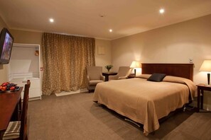 A hotel room with a bed, two chairs, a desk with fruit, a television, and a lamp. - Highfield Mews (Oamaru)