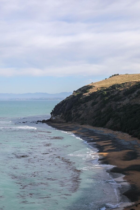 A coastal landscape with a beach, rocky cliffs, and a view of the sea. - Highfield Mews (Oamaru)
