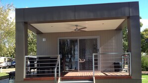 A modern building with a covered patio area, a staircase leading to a deck, and a fenced outdoor seating area. - Ski Club Holiday Park (Mulwala)