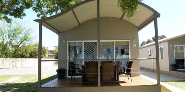A covered outdoor seating area with a table and chairs, a glass door, and a view of a residential street. - Ski Club Holiday Park (Mulwala)