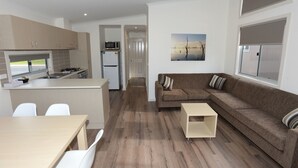 A modern kitchen with a microwave, refrigerator, and dining area. There is a brown sofa and a small table in the living area. - Ski Club Holiday Park (Mulwala)