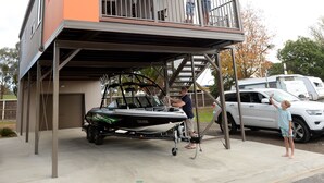 A two-story house with a balcony, a boat trailer, and a white SUV parked outside. - Ski Club Holiday Park (Mulwala)
